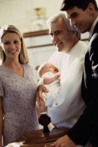 Young couple standing with a priest carrying their baby